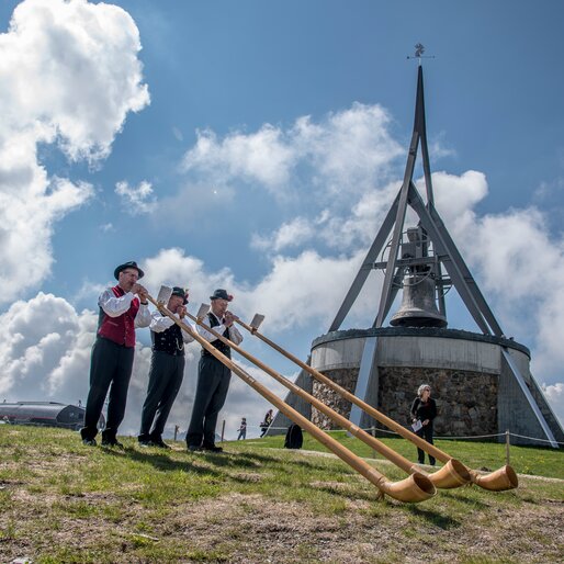 3 Alphornbläser spielen vor der Glocke Concordia 2000 am Kronplatz-Gipfel. | © Skirama Kronplatz