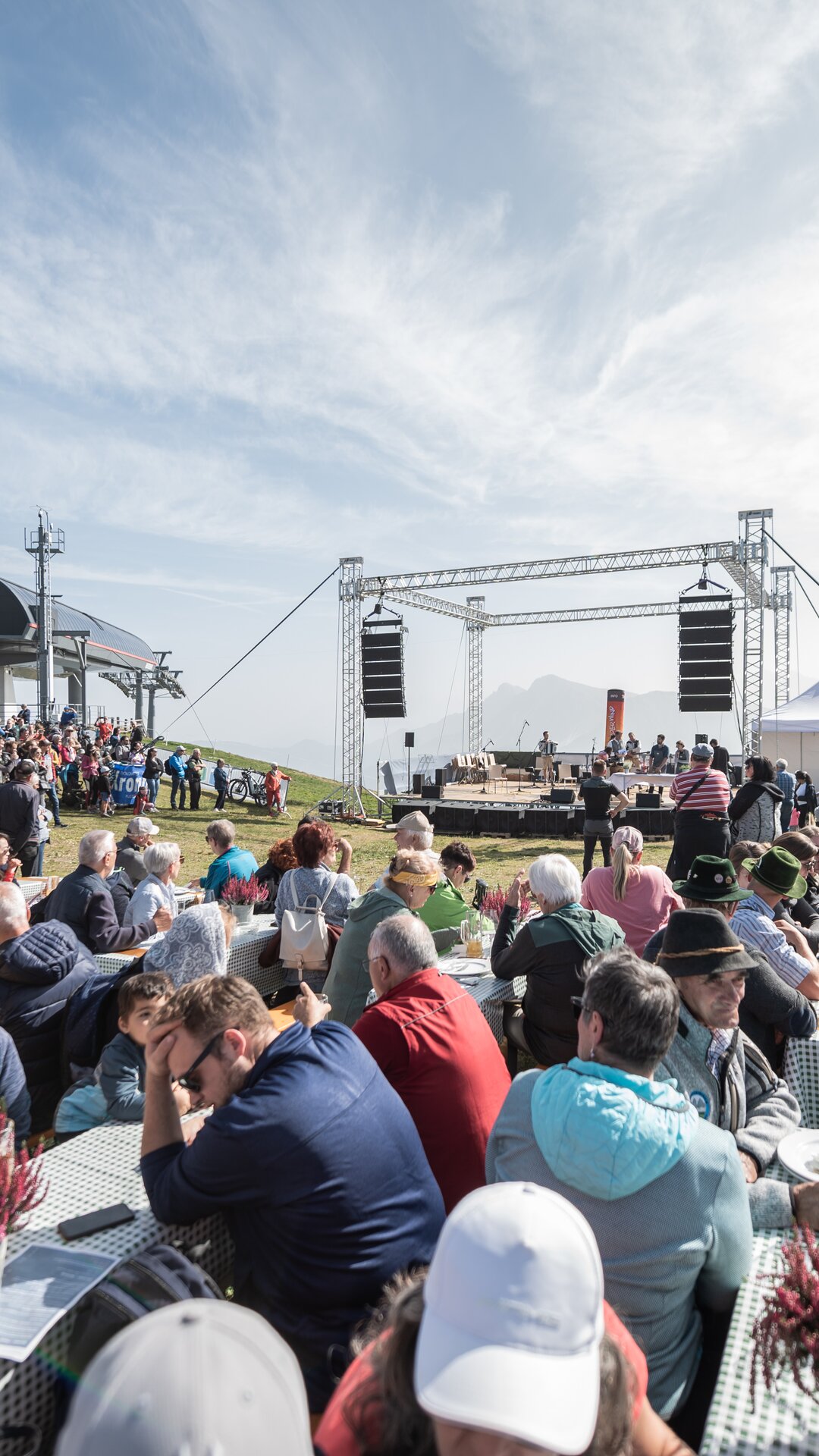 Zahlreiche Menschen sitzen an langen Tischen vor einer Bühne bei einer Freiluftveranstaltung. | © Gianvito Coco