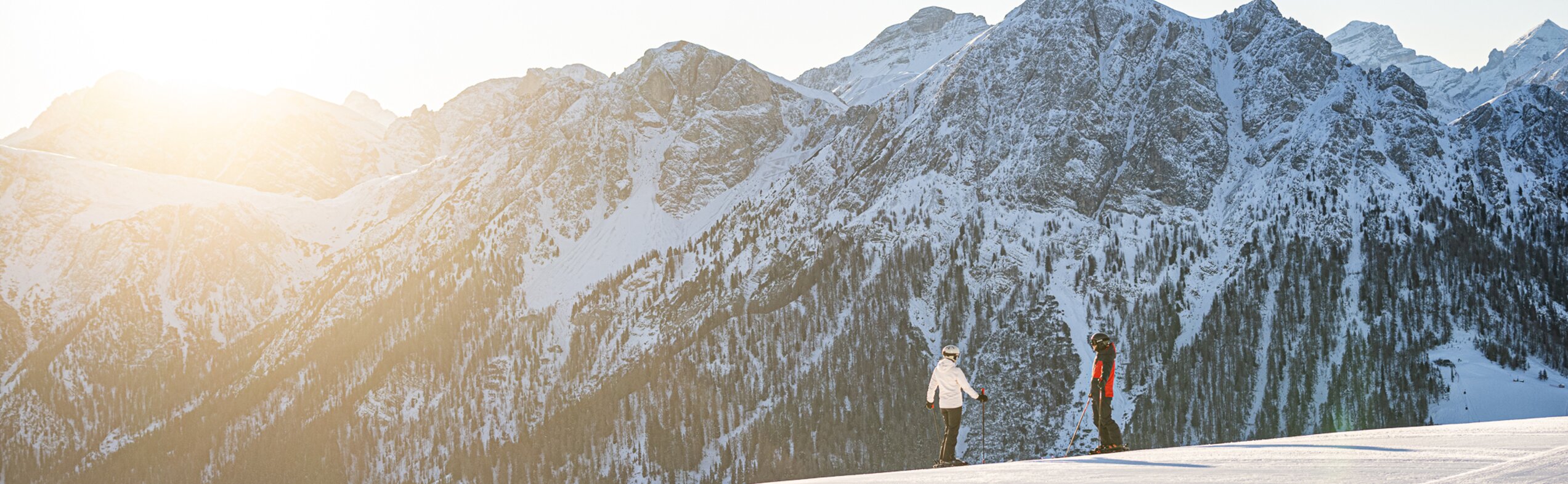 Zwei Skifahrer genießen die Aussicht auf strahlend weiße Berge und morgendlichem Licht. | © Harald Wisthaler