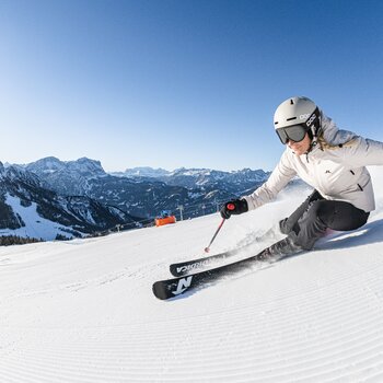 Skifahrerin fährt vor strahlend weißen Bergen und blauem Himmel die Piste hinunter. | © Harald Wisthaler